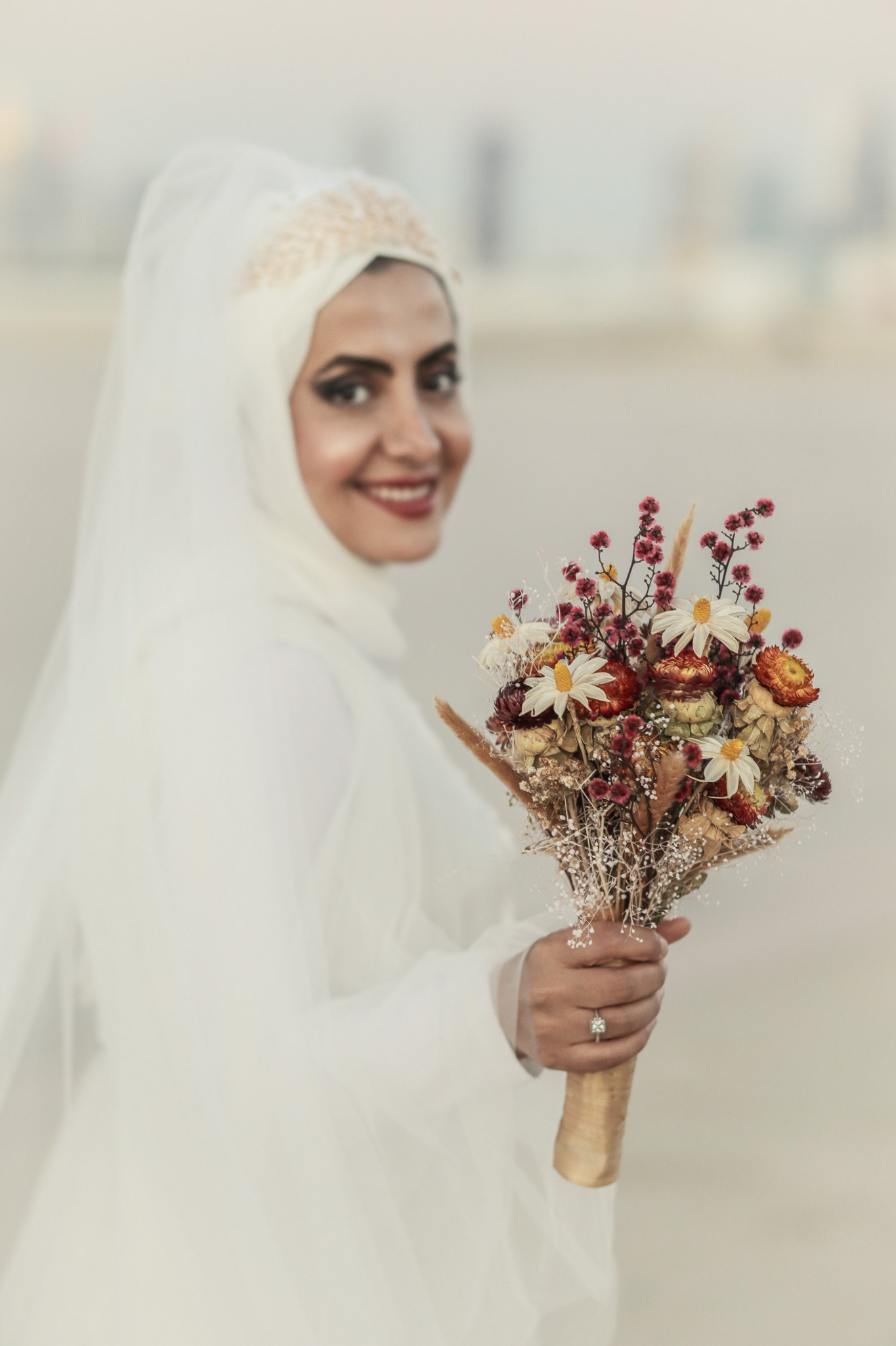Ein junges Brautpaar im Weiß und mit Hochzeitsblumen in der Hand sieht die Kamera - Hamid Afzali – Hochzeitsfotograf und Hochzeitsvideograf